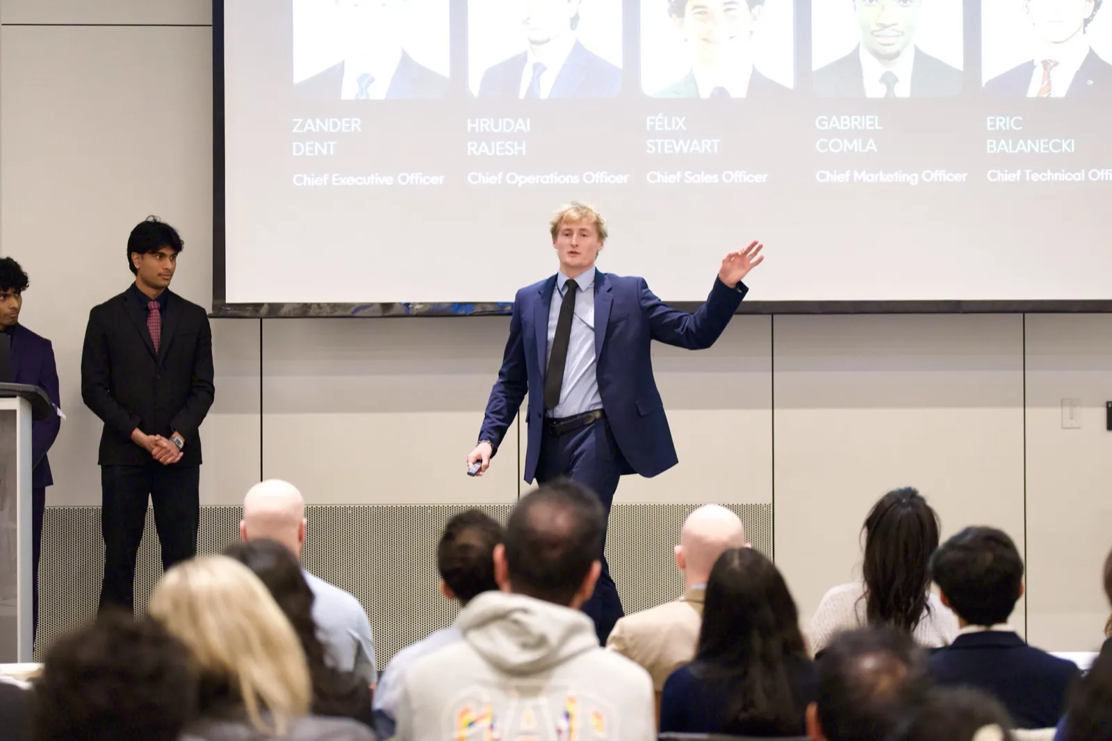 Zander Dent presenting on stage to a full lecture hall, founding team slide behind him
