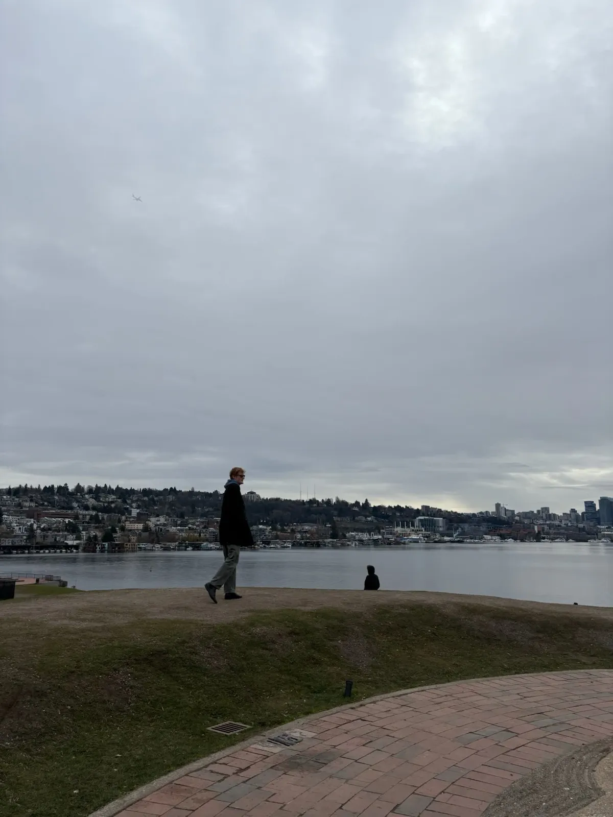 A figure walking a waterfront path under a wide overcast sky